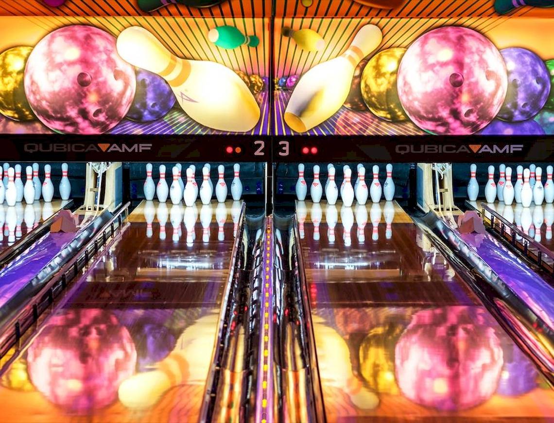 Eine Bowlingbahn mit bunten Bowlingkugeln und Kegeln, bunt beleuchtet.