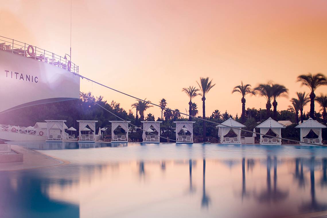Sonnenuntergang am Pool des Titanic Deluxe Lara Hotels mit Sonnenliegen und Palmen.