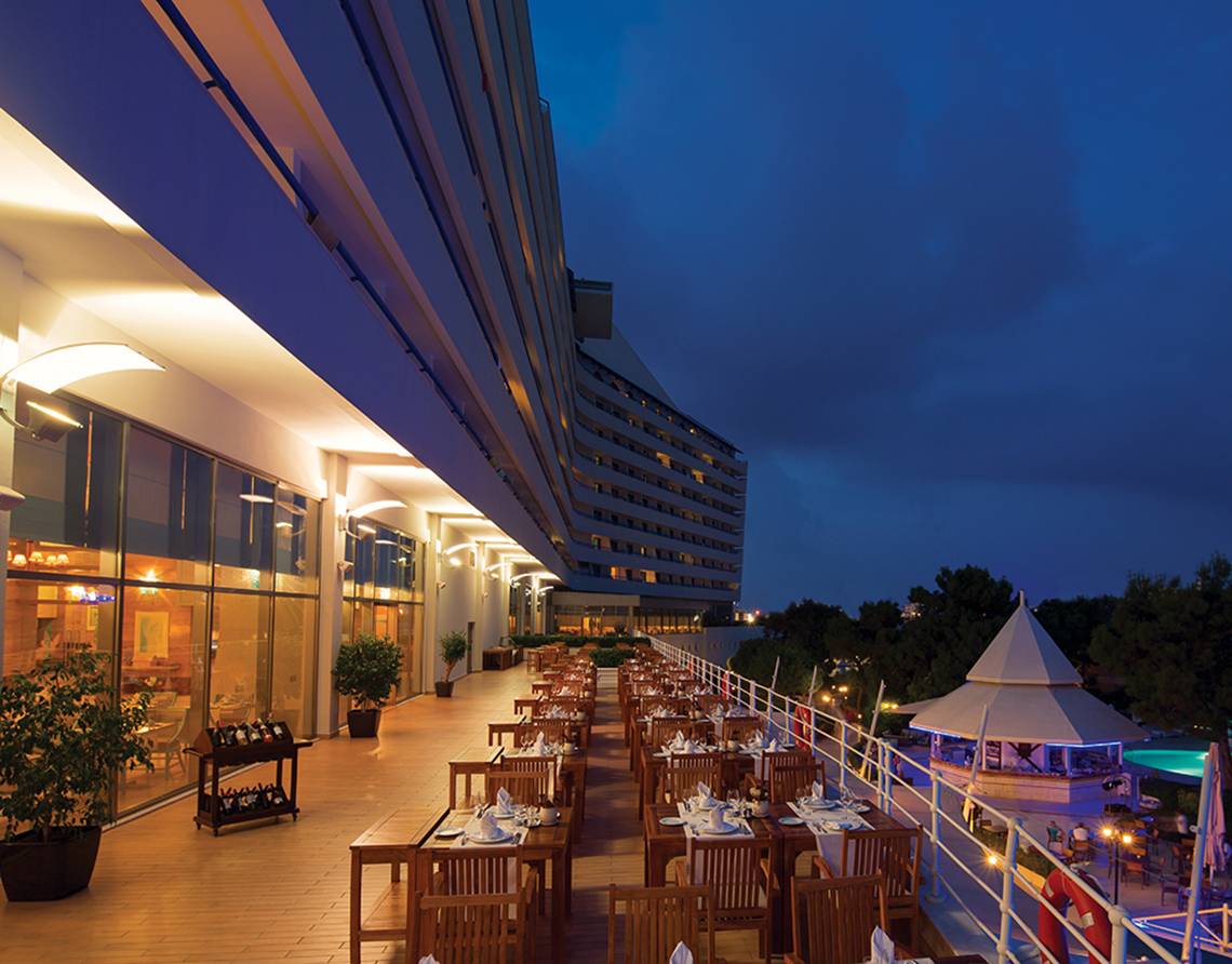 Abendliche Ansicht der Außenterrasse des Titanic Deluxe Lara Hotels mit gedeckten Tischen und Blick auf das Meer.