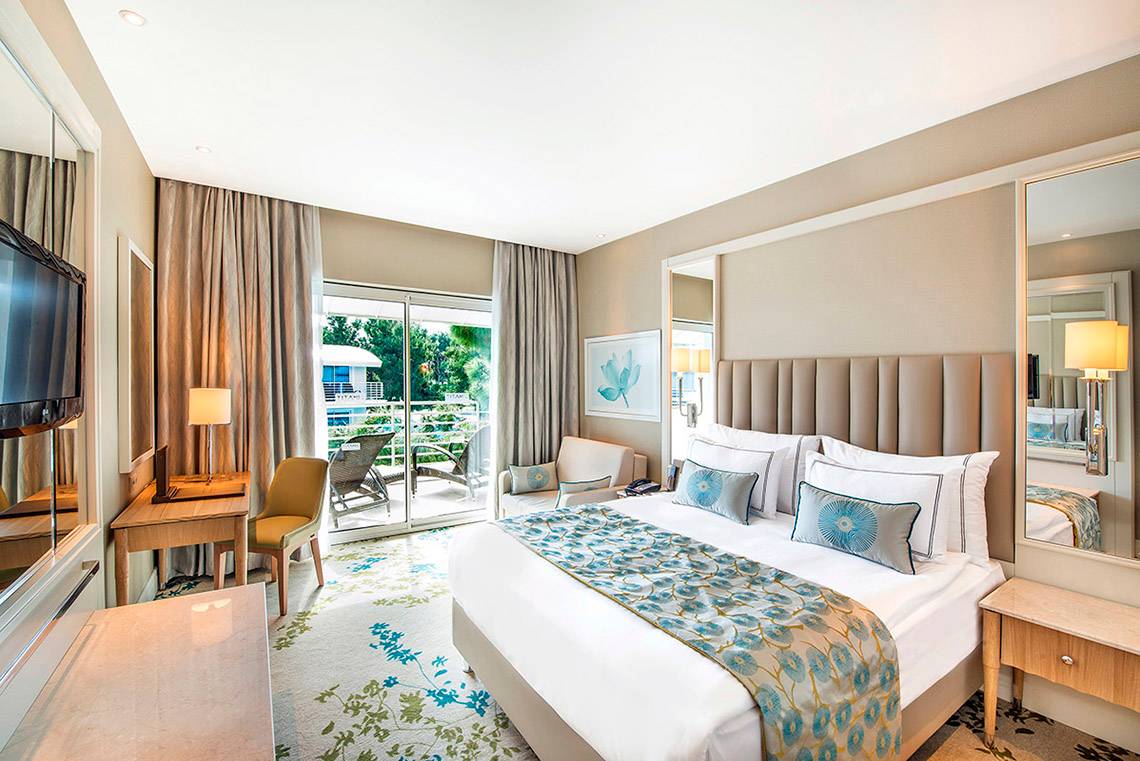 Ein elegantes Hotelzimmer im Titanic Deluxe Lara Hotel mit einem großen Bett, einem Balkon und einer Aussicht auf den Garten.