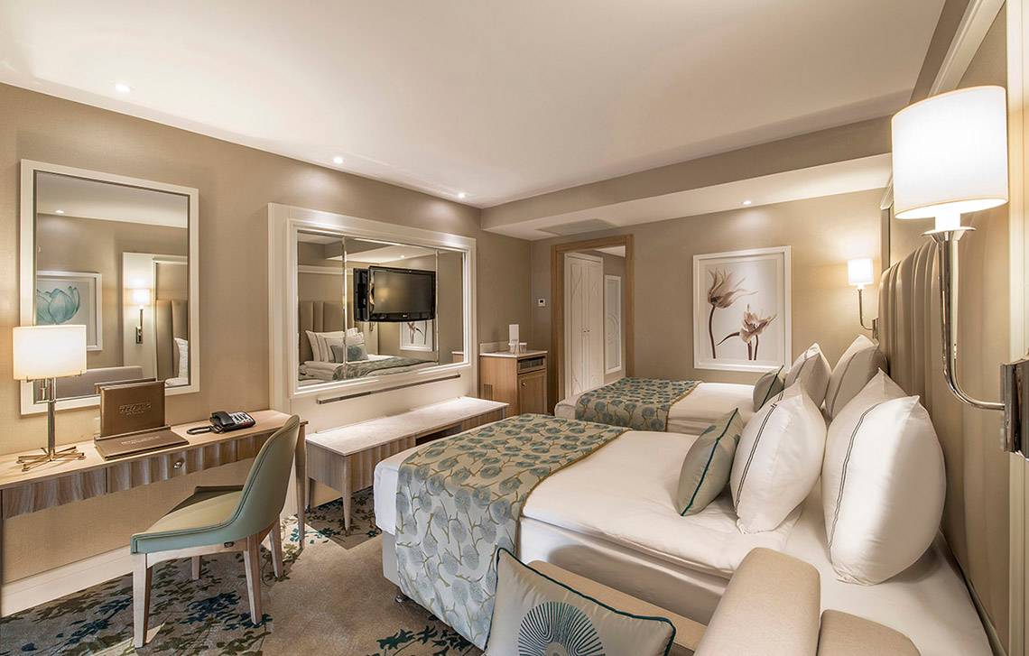 Hotelzimmer im Titanic Deluxe Lara mit zwei Betten, Schreibtisch, Spiegel und Fernseher.
