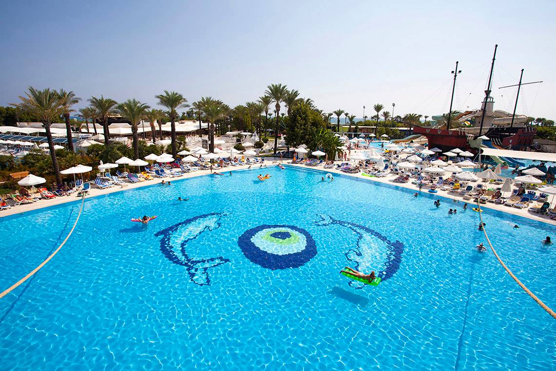 Ein großes Schwimmbad des Titanic Deluxe Lara Hotels mit vielen Gästen und einem Piratenschiff im Hintergrund.