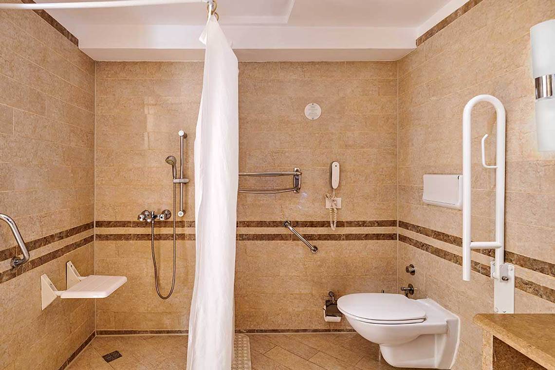 Barrierefreies Badezimmer im Hotel mit begehbarer Dusche, Toilette und Haltegriffen.