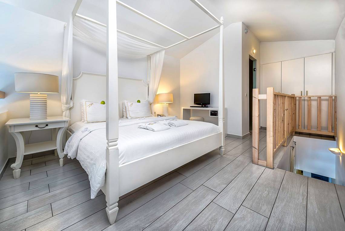 Schlafzimmer im Diamond Deluxe Hotel mit einem großen Bett, weißem Überwurf und Vorhängen.