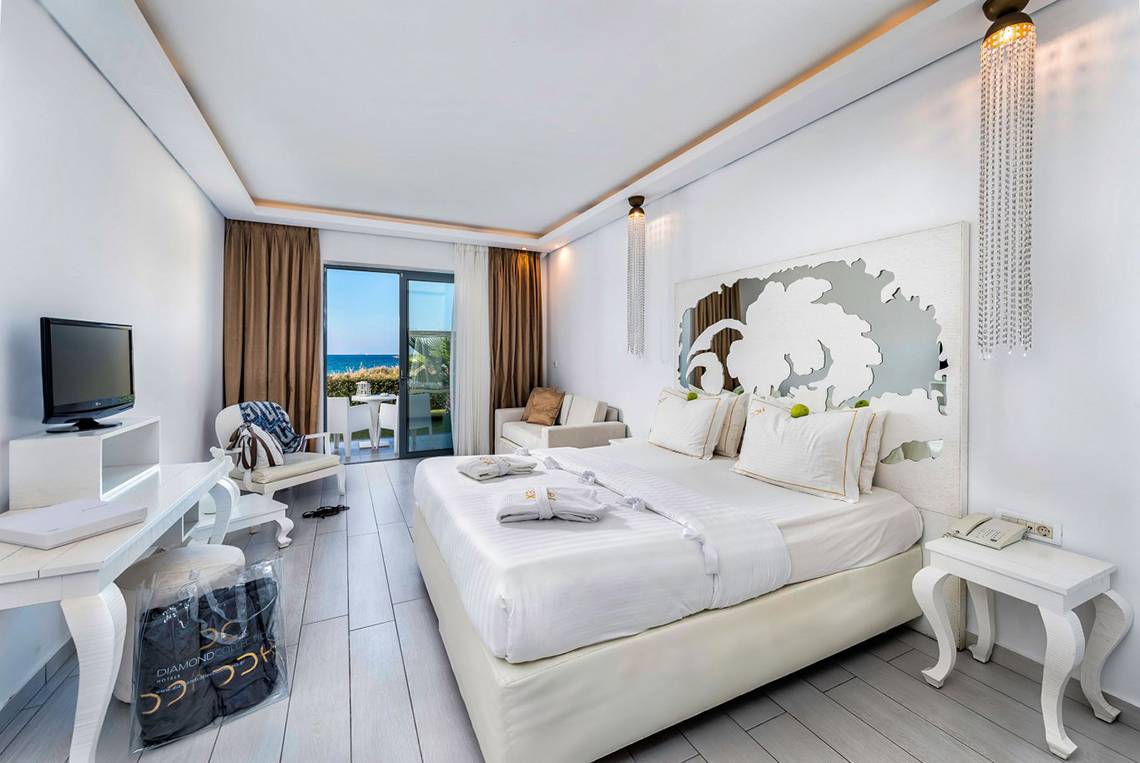 Innenansicht eines Zimmers im Diamond Deluxe Hotel mit einem großen Bett, Fernseher, Schreibtisch und Balkon.