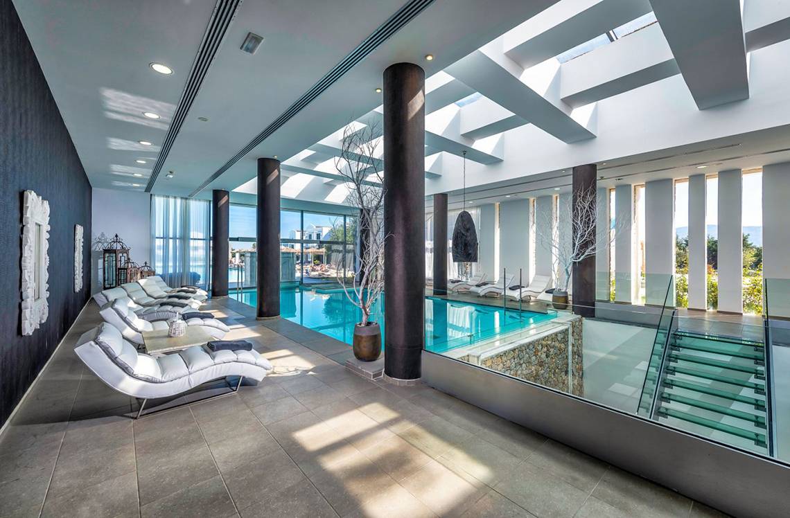 Innenpool-Loungebereich im Diamond Deluxe Hotel mit weißen Liegestühlen und Glaswänden.