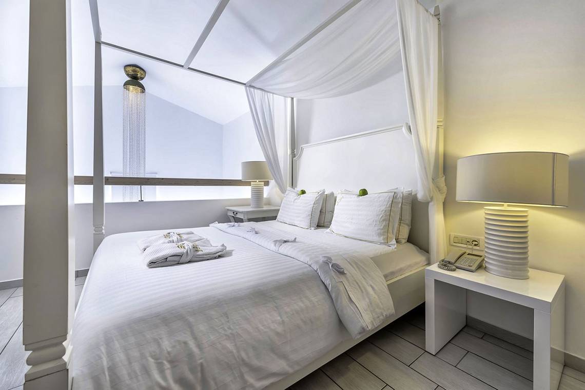 Innenansicht des Schlafzimmers im Diamond Deluxe Hotel mit vierposterbett, weißen Vorhängen und modernen Lampen.