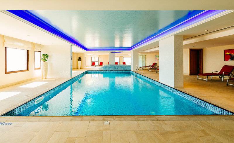 Innenpool des Marjan Island Resort & Spa mit blauen Beleuchtung und Lounge-Bereich.