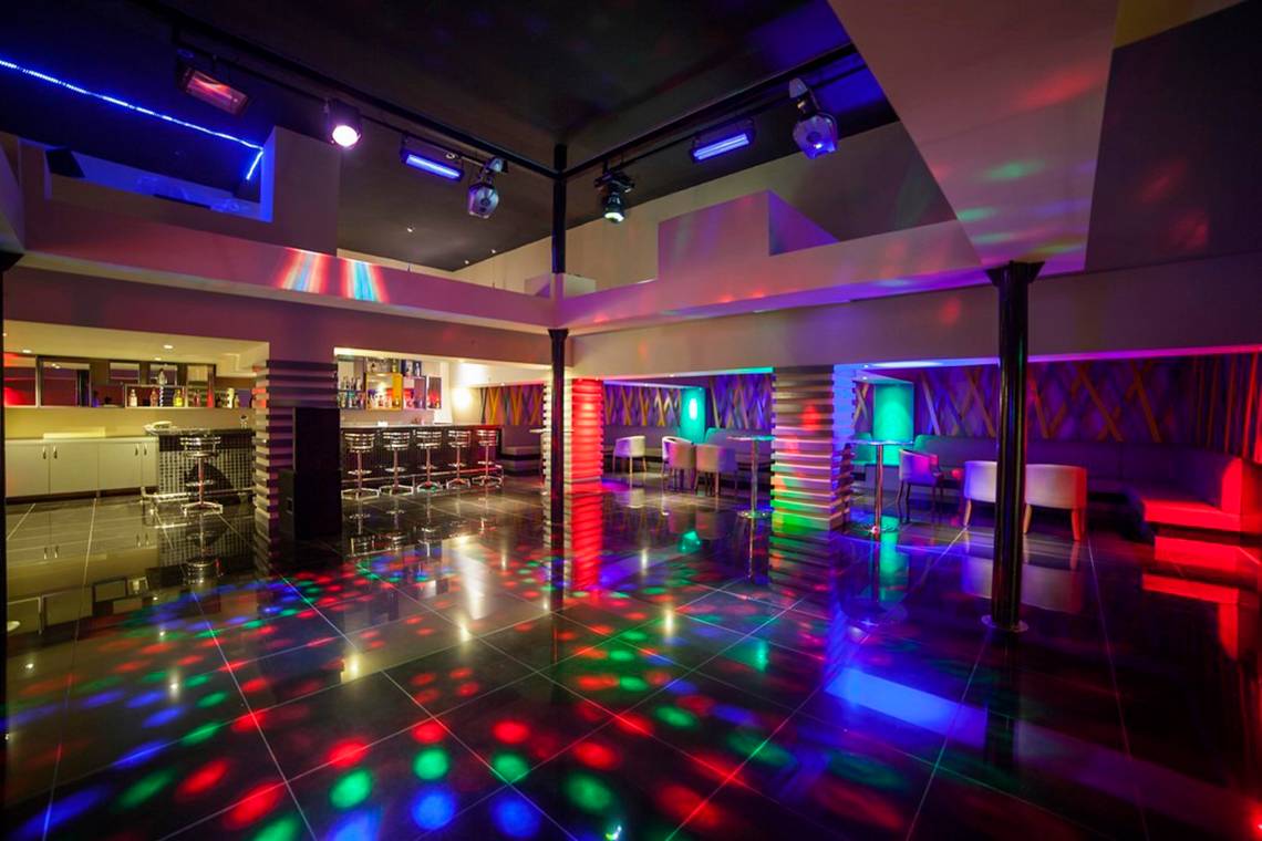 Innenansicht des Disco-Saals im Arcanus Side Resort Hotel mit farbigen Lichtern und Sitzbereichen.