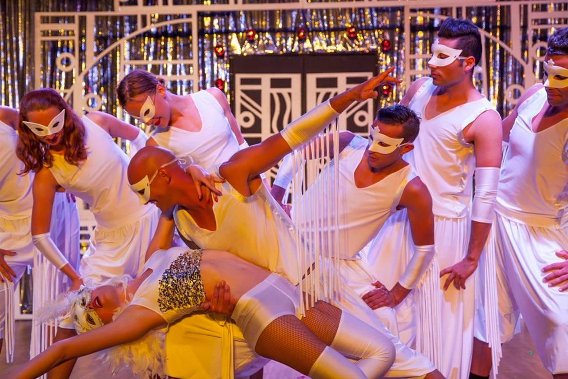 Tanzgruppe in weißen Kostümen mit Masken, die eine Choreografie aufführen.