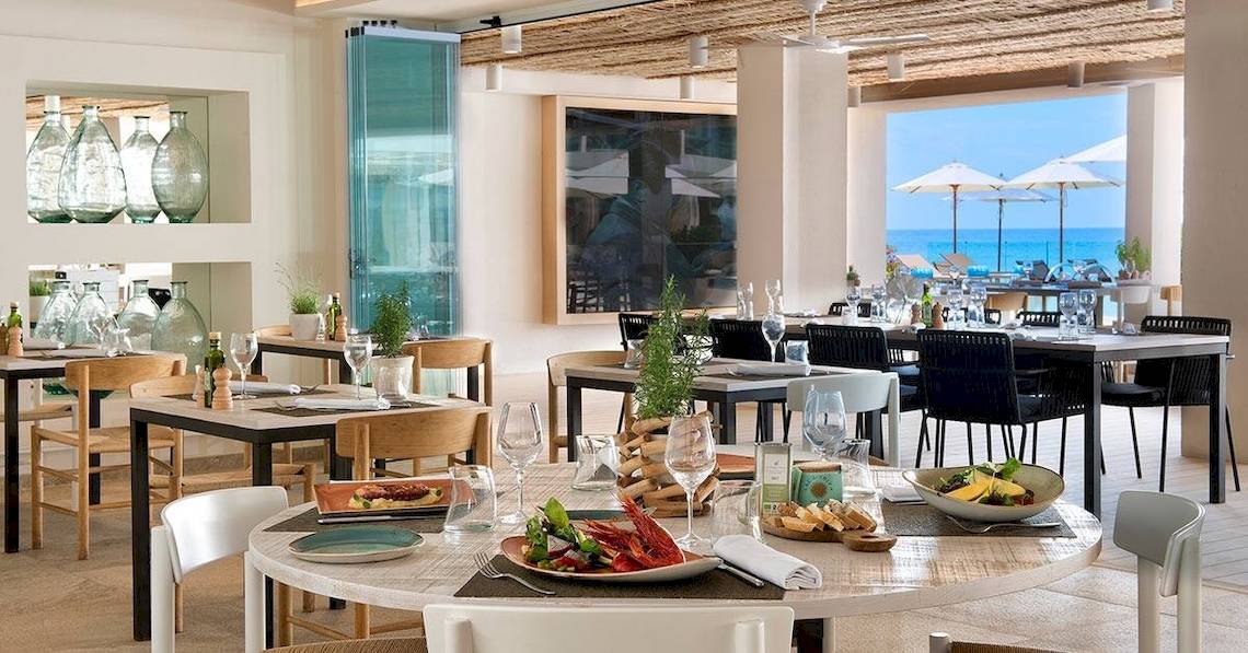 Innenbereich des ME Ibiza Hotels mit Blick auf das Meer und einem Esstisch mit Speisen.