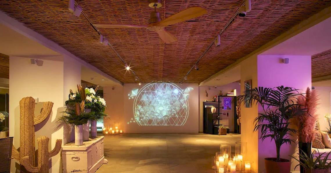Innenraum des ME Ibiza Hotels mit Loungebereich, Projektion an der Wand, Pflanzen und Kerzen.