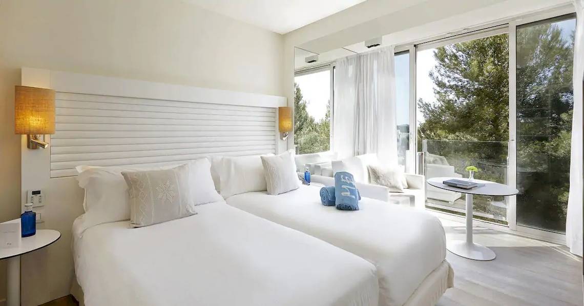 Doppelzimmer im ME Ibiza Hotel mit zwei weißen Betten, Kissen und Ausblick auf den Garten