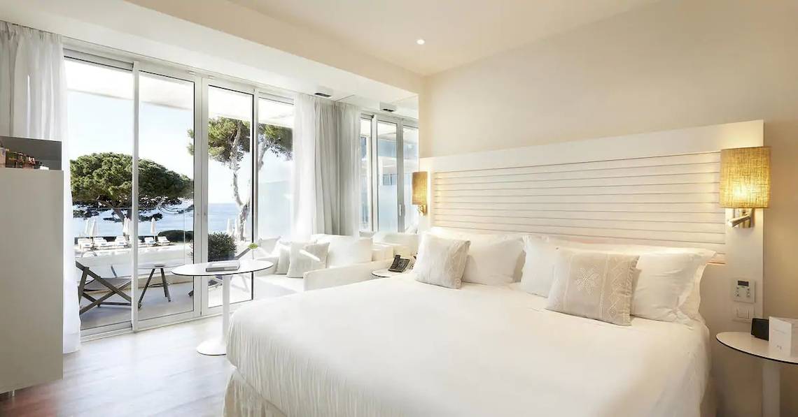 Innenansicht eines Zimmers im ME Ibiza Hotel mit Meerblick, inklusive eines großen Bettes und eines Tisches mit einer Telefon.