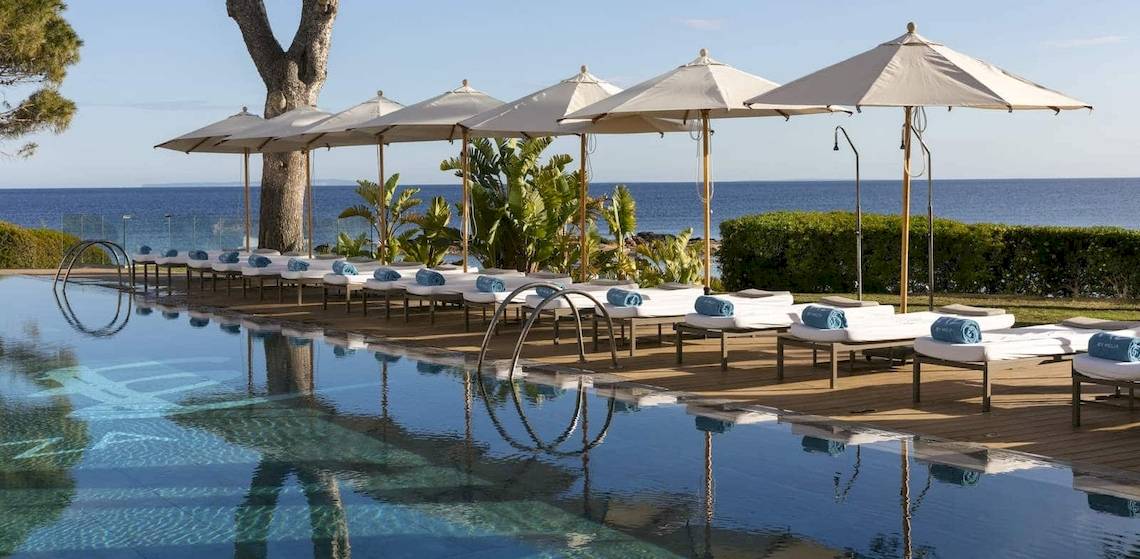 Poolbereich des ME Ibiza Hotels mit Sonnenliegen und Sonnenschirmen am Meer
