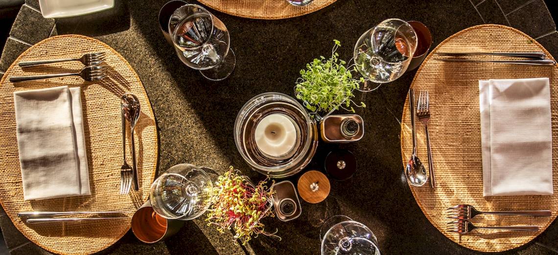 Ein Tisch im Dinarobin Beachcomber Golf Resort & Spa, mit Tellern, Besteck, Gläsern und einer Kerze dekoriert.