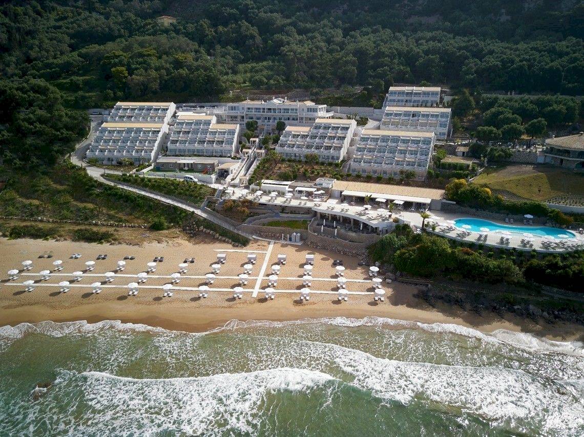 Luftaufnahme des Pelekas Klosters an der Strandpromenade mit vielen Sonnenschirmen.