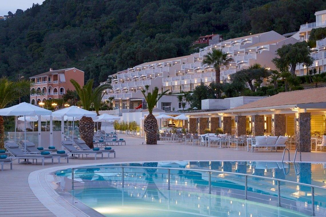 Pelekas Monastery Hotel Pool-Ansicht bei Nacht mit Lounge-Stühlen, Sonnenschirmen und Berg im Hintergrund