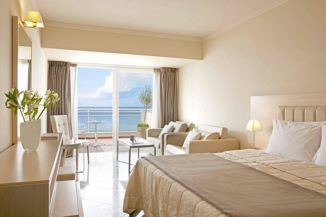 Hotelzimmer im Pelekas Kloster mit Balkon und Meerblick, modernes Design, weiße Möbel und Pflanzen.