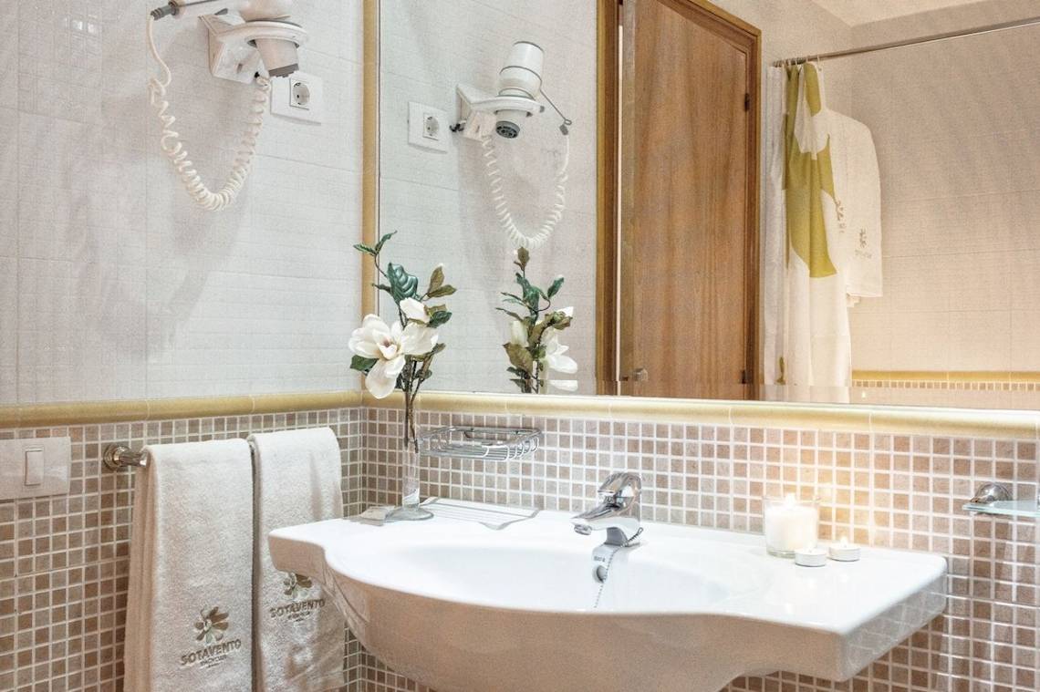 Badezimmer des Sotavento Beach Club Hotels mit gefliester Wand, Waschbecken und Spiegel.