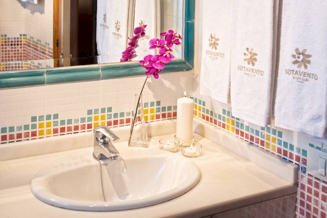 Badezimmer mit Waschbecken, Spiegel und bunten Kacheln im Sotavento Beach Club Hotel.