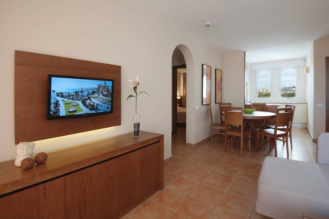 Wohnzimmer im Sotavento Beach Club mit Fernseher, Blumenvase und Esstisch.