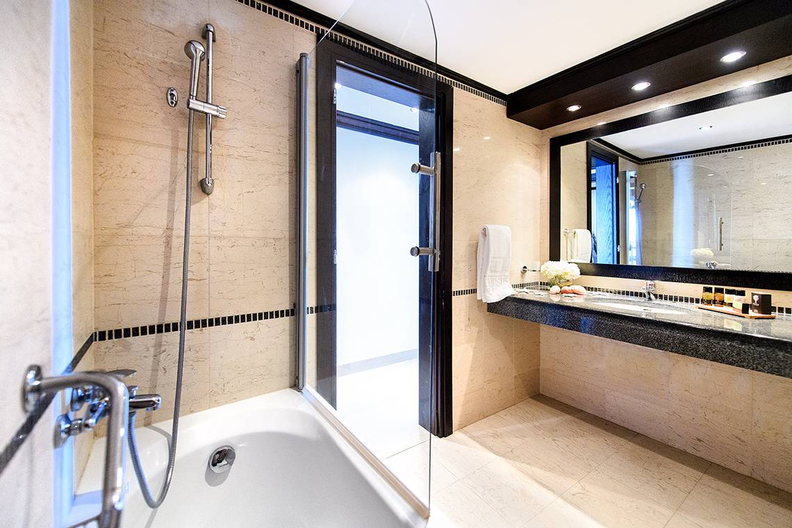 Badezimmer im Mitsis Faliraki Beach Hotel & Spa mit Badewanne, Glastür, Spiegel und Waschbecken