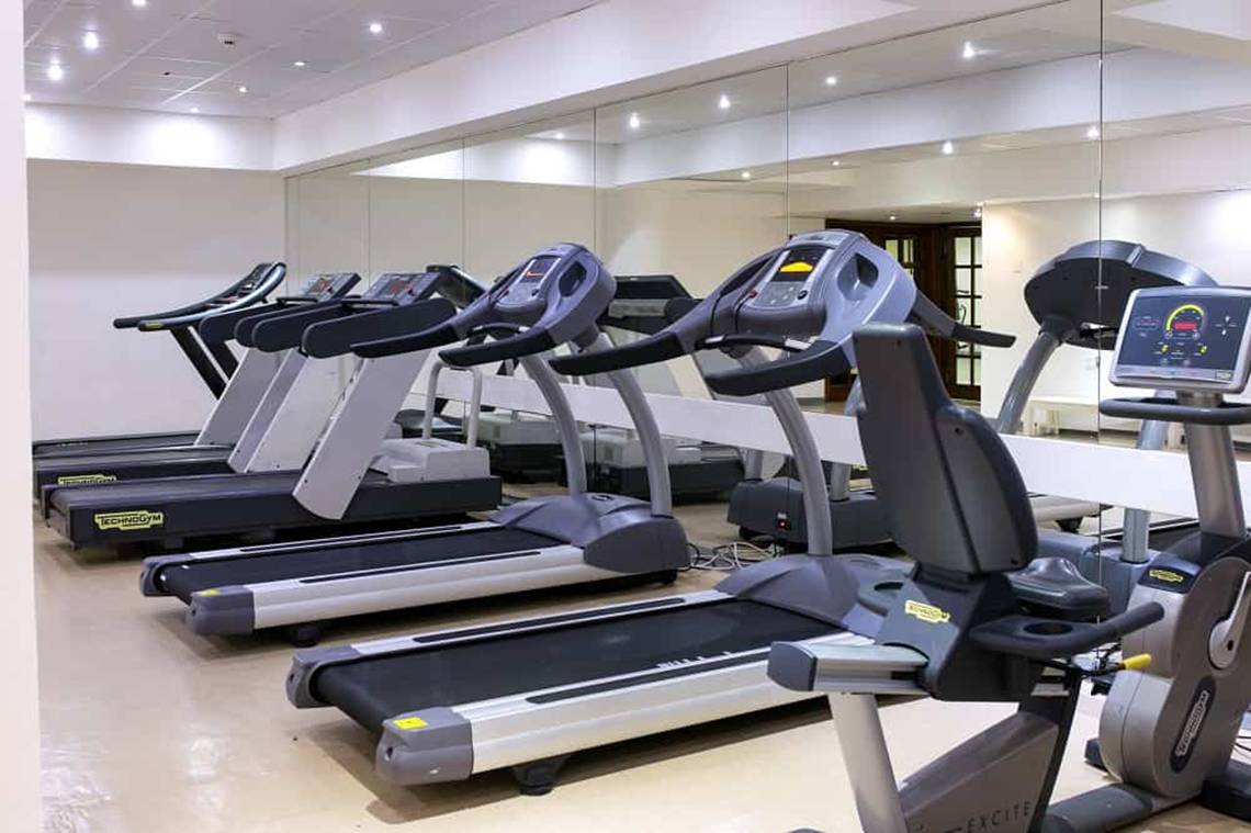 Fitnessstudio im Golden Bay Beach Hotel mit mehreren schwarzen und grauen Laufbändern.