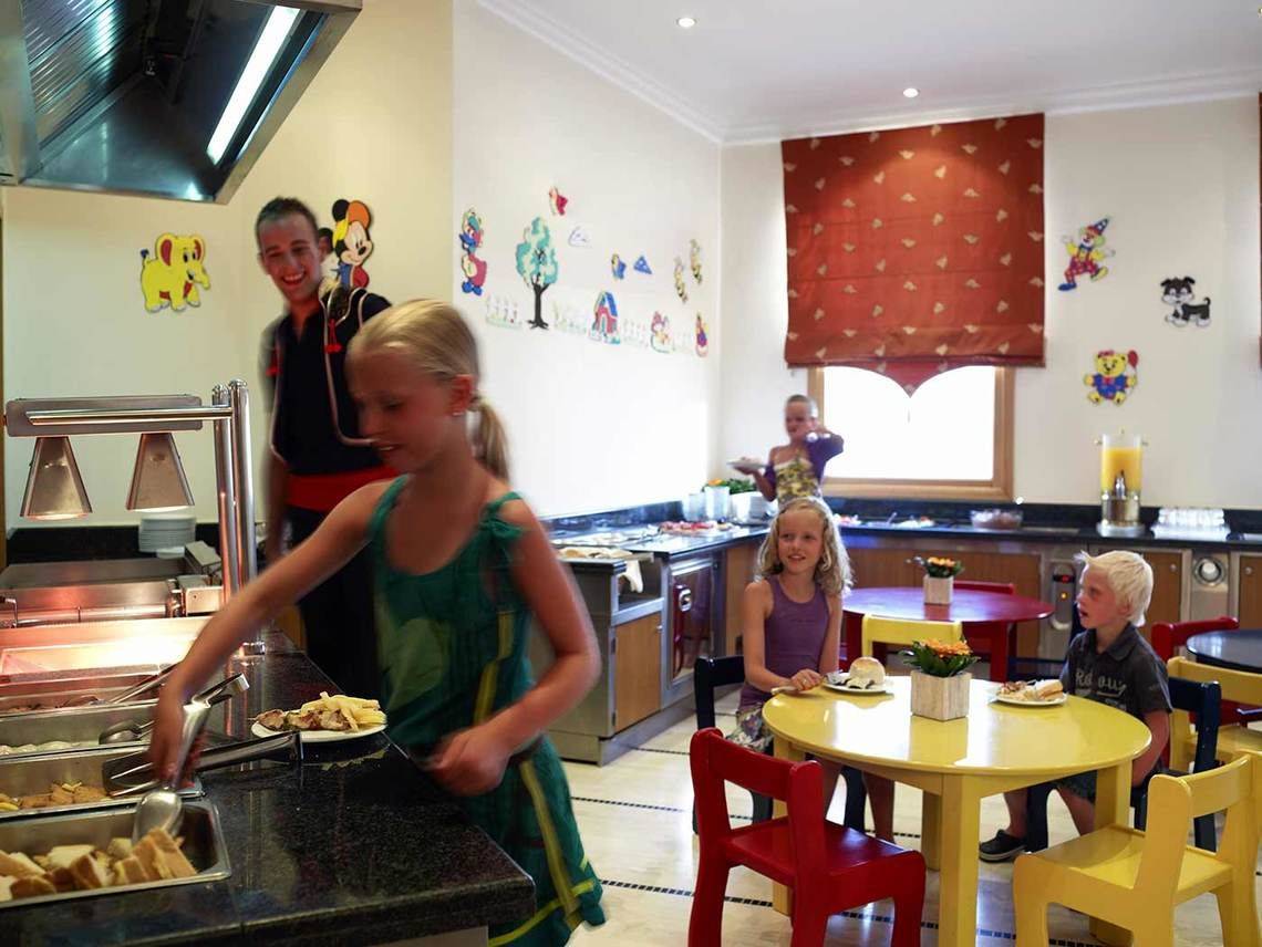 Frühstücksbuffet im Mitsis Rinela Beach Hotel mit Kindern, die Speisen servieren.