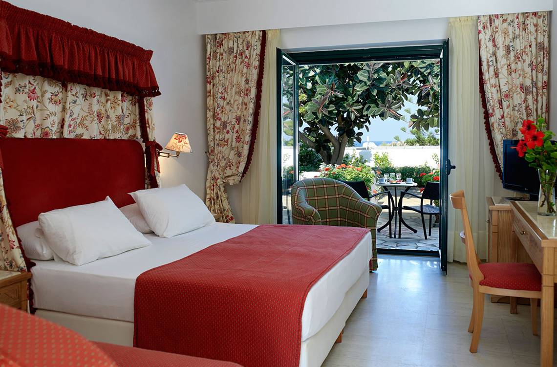 Zimmer im Mitsis Rinela Beach Hotel mit Blick auf eine Terrasse und einen Garten.