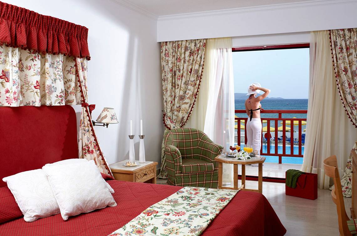 Zimmer im Mitsis Rinela Beach Hotel mit Blick auf den Balkon und das Meer.