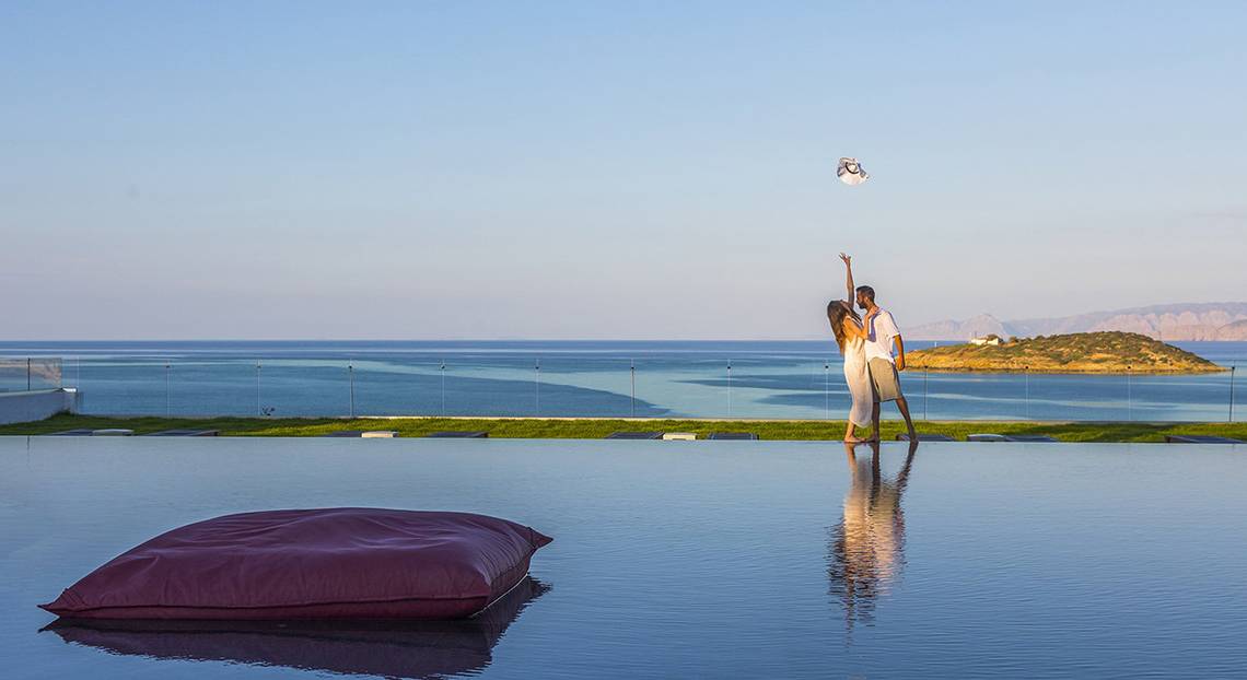 Paar im Minos Palace Hotel & Suites am Strand, das nach einem Frisbee greift, mit Blick auf das Meer.