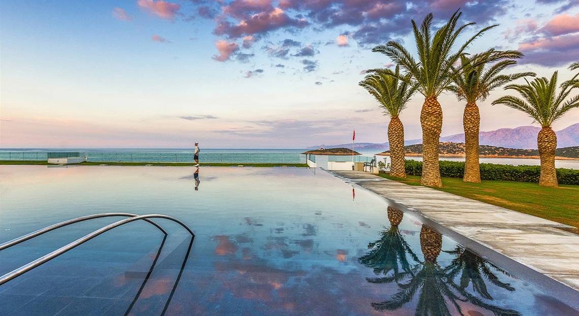 Außenpool des Minos Palace Hotel & Suites bei Sonnenuntergang mit Palmen und Meerblick