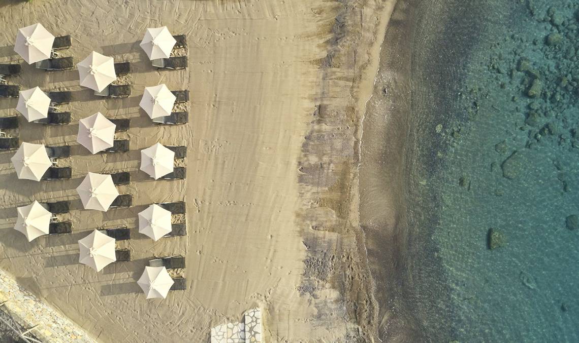 Luftaufnahme von Liegestühlen und Sonnenschirmen am Strand des Minos Palace Hotel & Suites.