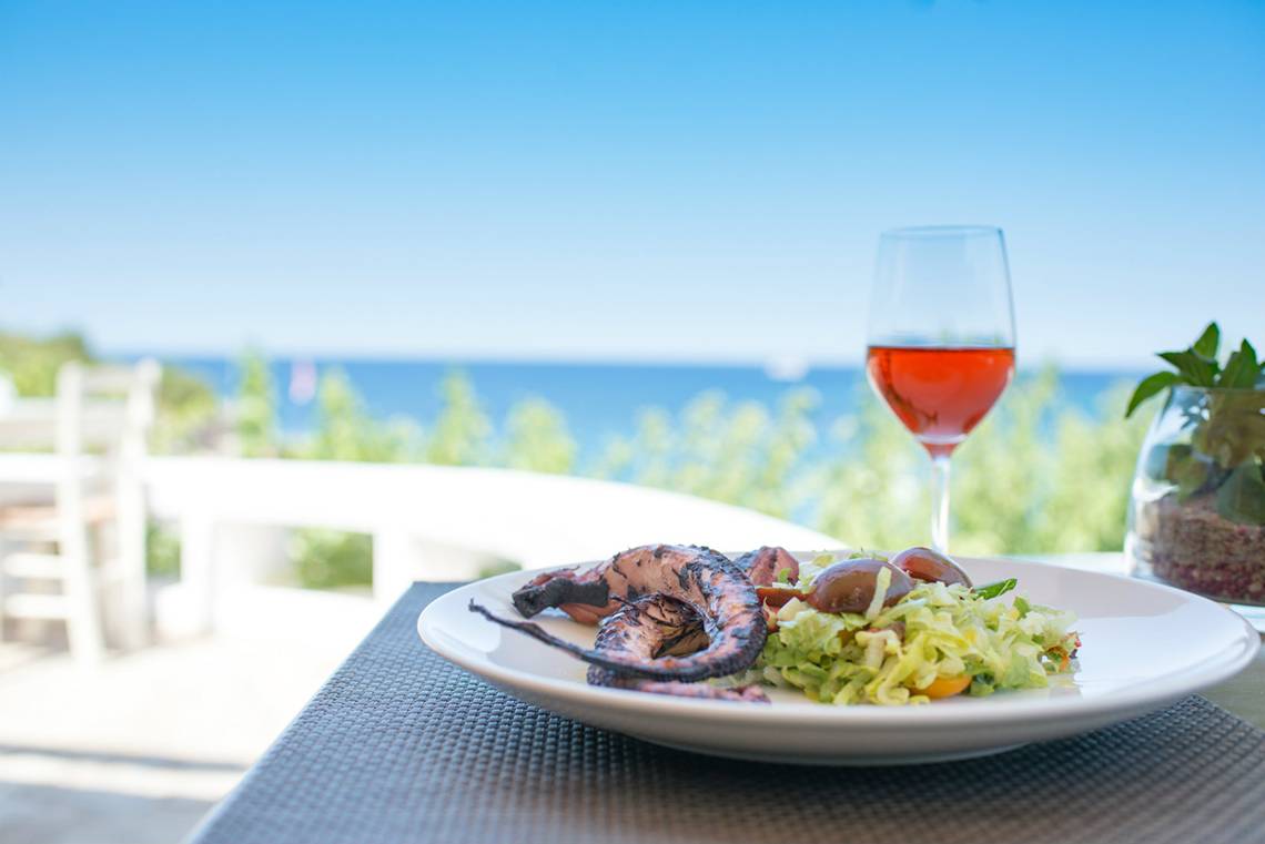 Eine Terrasse mit einem Teller Essen und einem Glas Wein im Minos Palace Hotel.