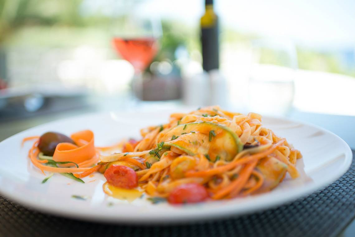 Gerecht auf einem weißen Teller mit Nudeln, Tomaten und Gemüse.
