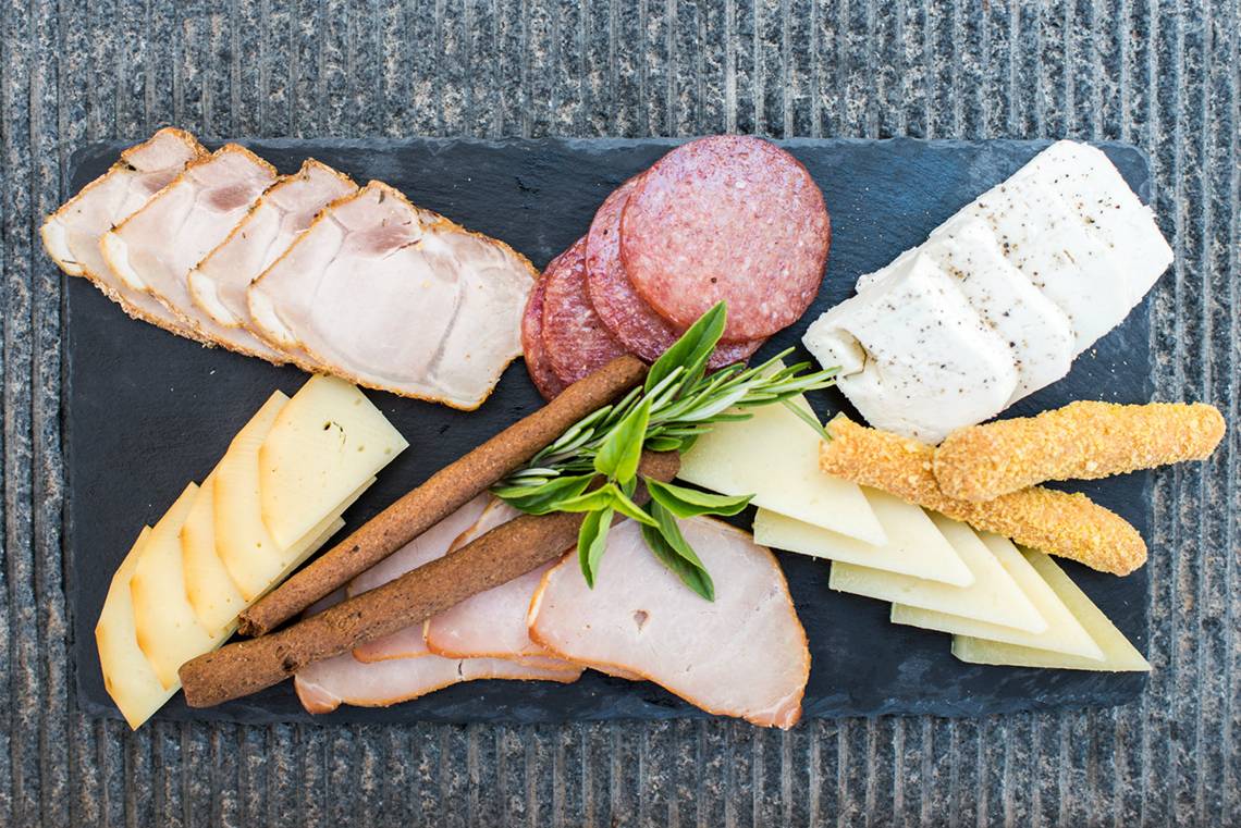 Eine Platte mit verschiedenen Fleischsorten, Käse und Kräutern auf einem schwarzen Untergrund.