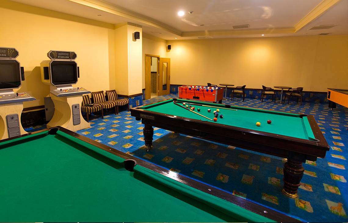 Spielzimmer im Side Sun Hotel mit zwei Billardtischen, Spielkonsolen und Tischen.