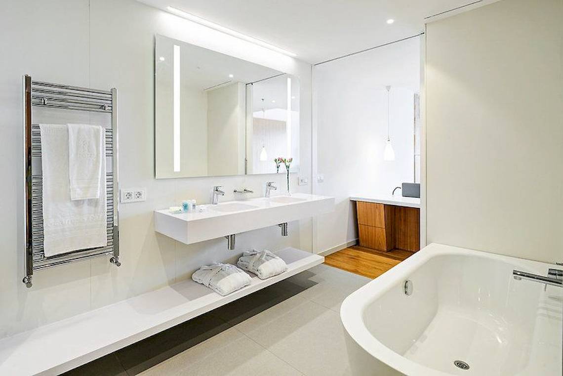 Ein modernes Badezimmer mit einem großen Spiegel, zwei Waschbecken, einer Badewanne, einem Handtuchwärmer und Holzboden.