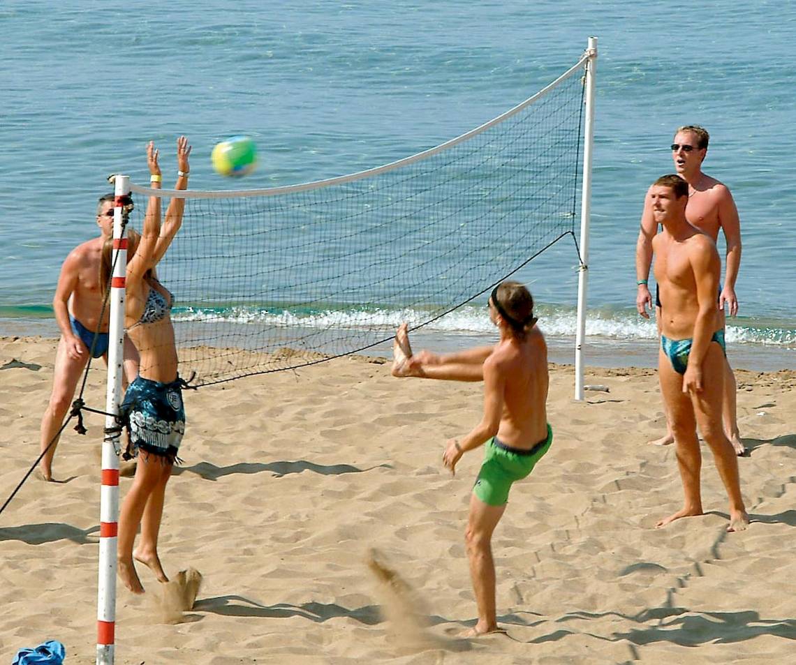 Gruppe junger Männer und Frauen spielt Volleyball am Strand in der Nähe des Wassers