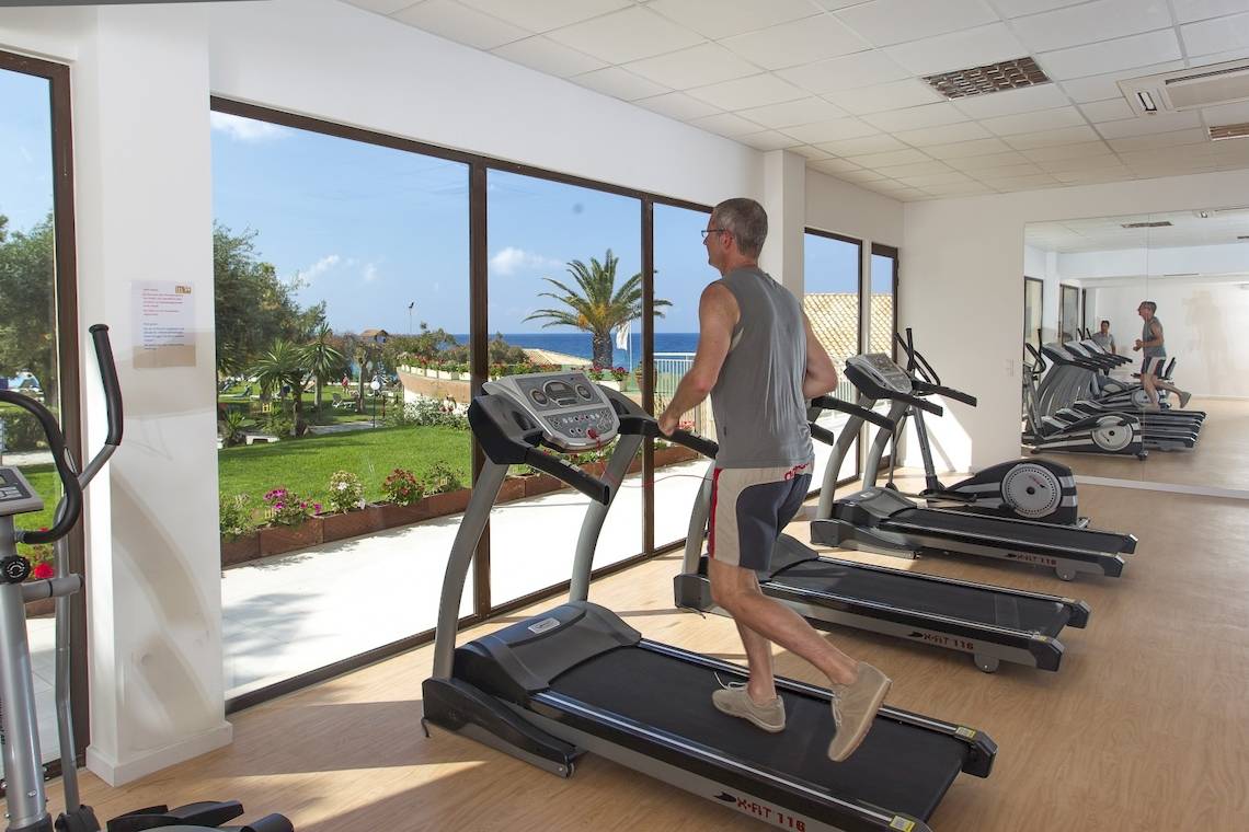 Ein älterer Mann läuft auf einem Laufband im Fitnessstudio mit Blick auf das Meer.