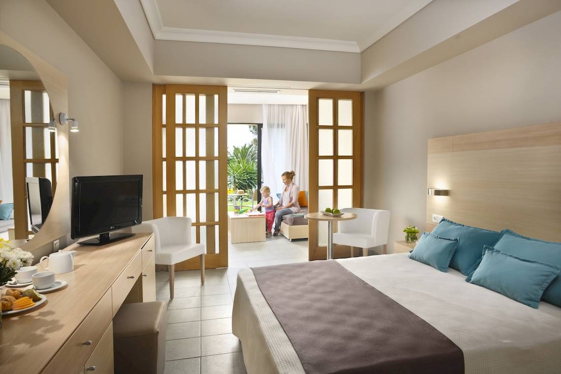 Hotelzimmer im Domes of Corfu, Autograph Collection mit Fernseher, Bett und Wohnzimmerbereich.