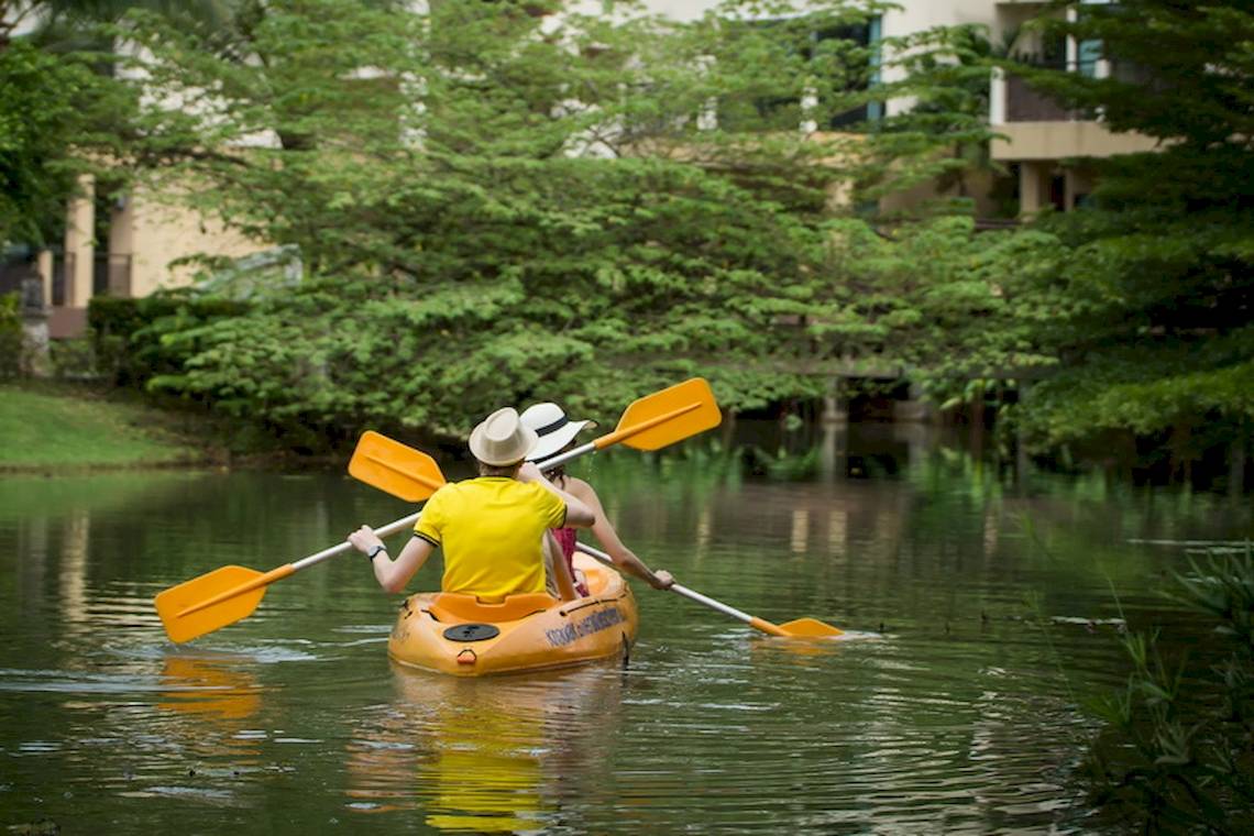 Zwei Leute im Kajak auf einem Fluss mit Gebäuden und Bäumen im Hintergrund