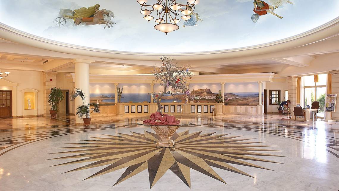 Lobby des Lindos Princess Beach Hotels mit einer großen Lichtkrone, einer zentralen Pflanzenvase und einer gemusterten Decke.
