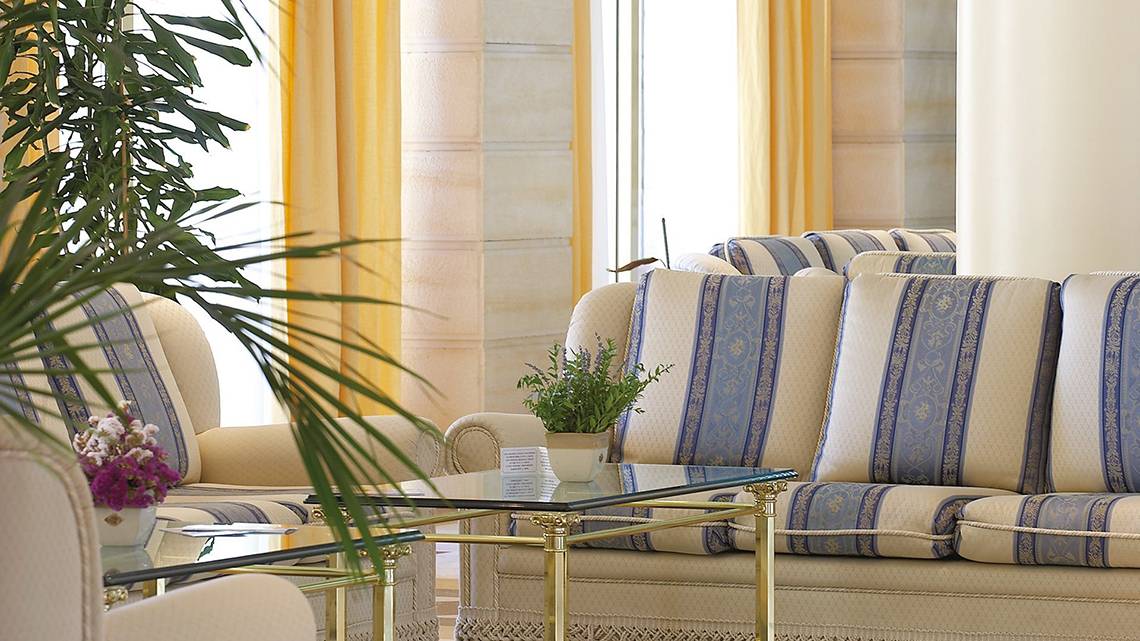 Loungebereich im Lindos Princess Beach Hotel mit blau-weiß gestreiften Sofas und Glastisch.