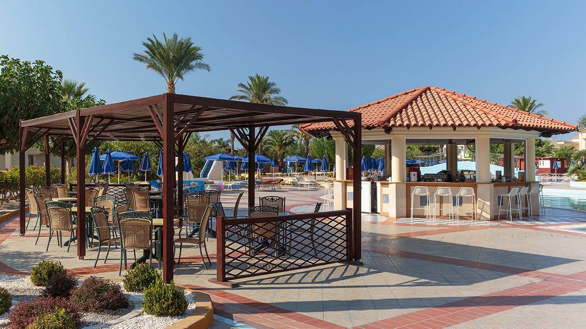 Terrasse des Lindos Princess Beach Hotels mit Tischen, Stühlen und Sonnenschirmen neben einem Barbereich.