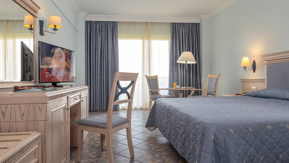 Ein Hotelzimmer im Lindos Princess Beach Hotel mit Bett, Schreibtisch, Fernseher und Möbeln.
