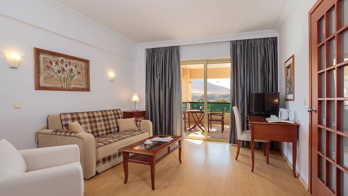Innenansicht eines Zimmers im Lindos Princess Beach Hotel mit einem Sofa, einem Tisch und einem Fernseher.