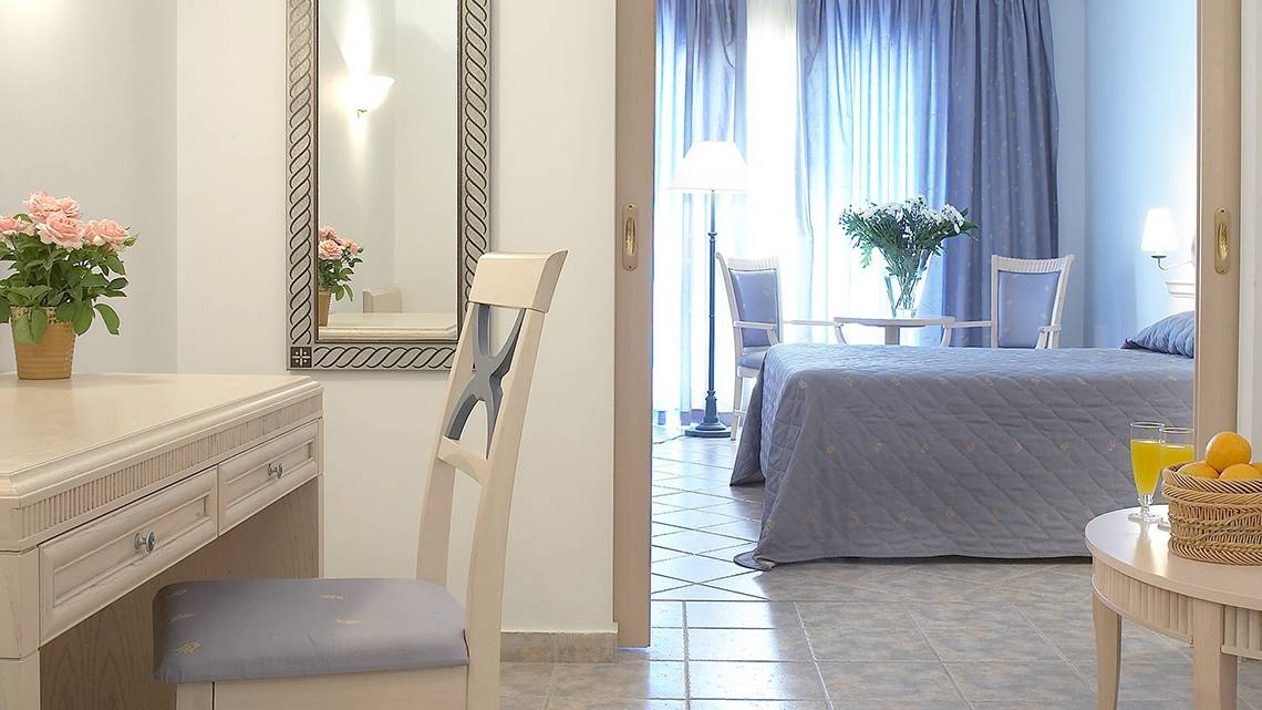 Innenansicht eines Zimmers im Lindos Princess Beach Hotel mit Bett, Schreibtisch und Möbeln.