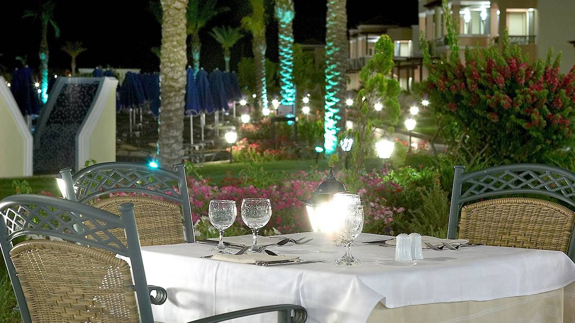 Außenbereich des Lindos Princess Beach Hotels mit beleuchtetem Tisch und Stühle.